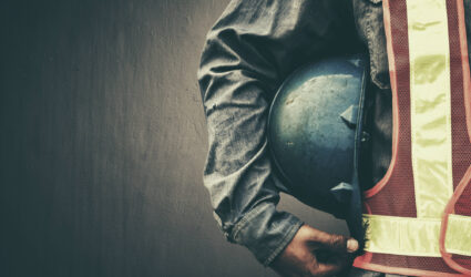 Worker in safety gear holding a construction helmet