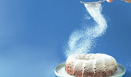 A person sifts icing sugar onto a cake in a swirling motion