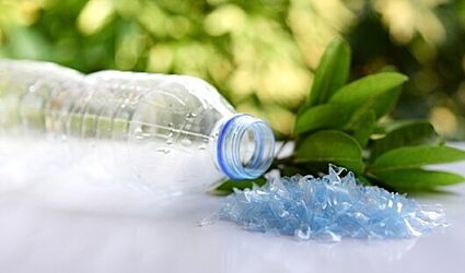 Plastic bottle next to plastic flakes and a bundle of leaves