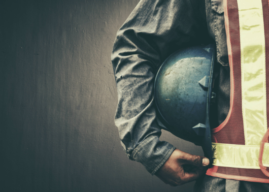 Worker in safety gear holding a construction helmet