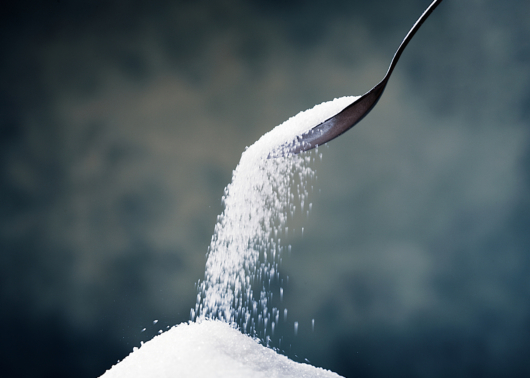 A stream of white sugar falling from a spoon