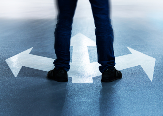 Man's legs standing on arrows pointing in three directions.