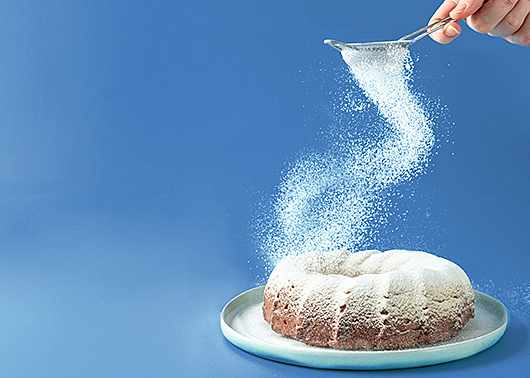 A person sifts icing sugar onto a cake in a swirling motion