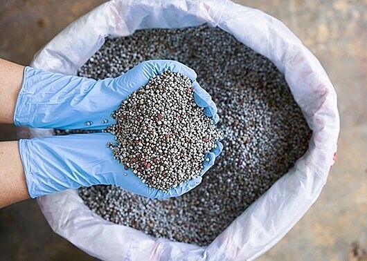 Gloved hands scooping fertilizer mix out of a bag