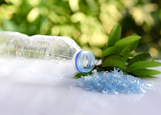 Plastic bottle next to plastic flakes and a bundle of leaves