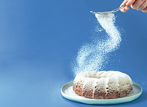 A person sifts icing sugar onto a cake in a swirling motion