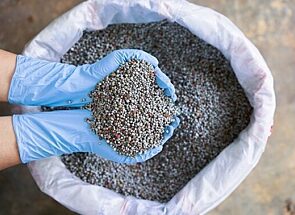Gloved hands scooping fertilizer mix out of a bag